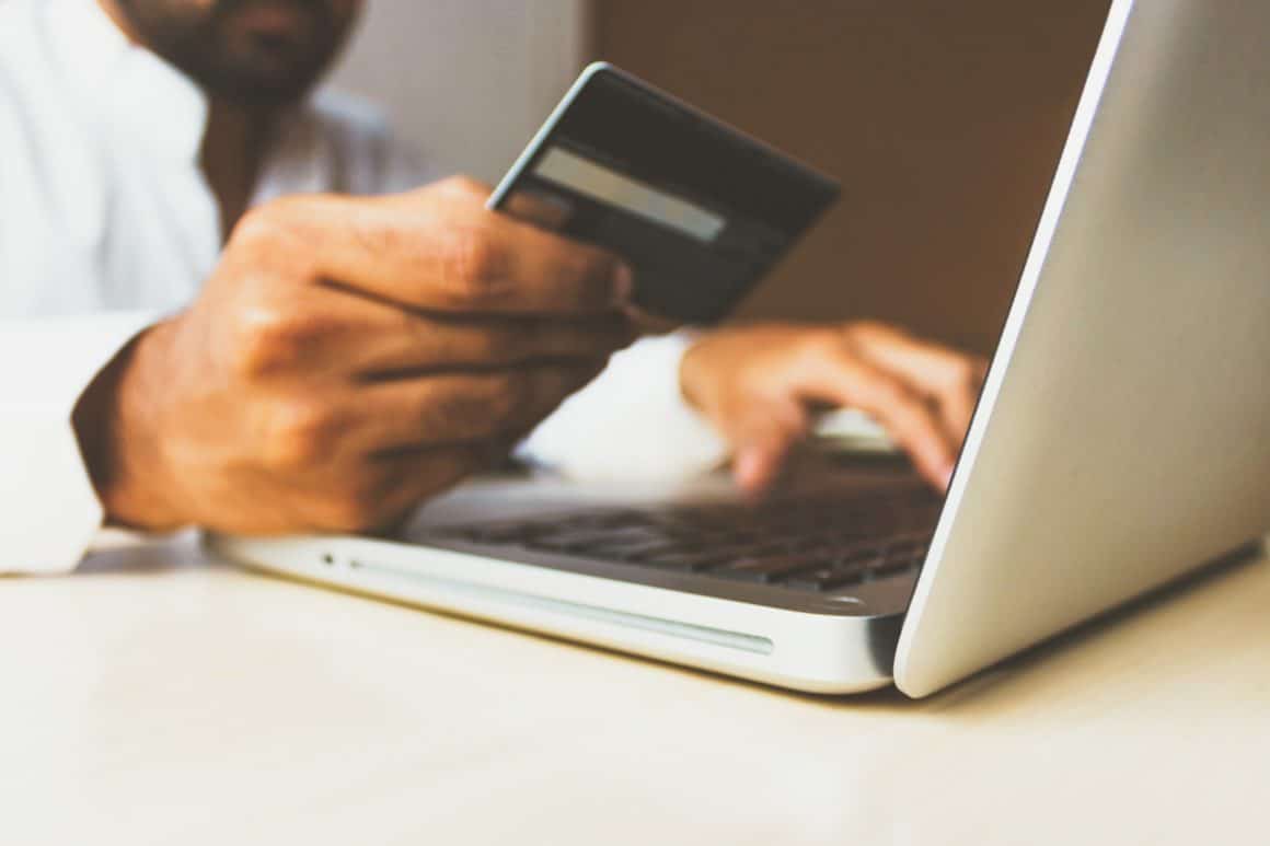 Photo of man typing on computer while holding credit card